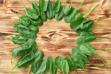 Frame made of fresh spinach leaves on wooden background