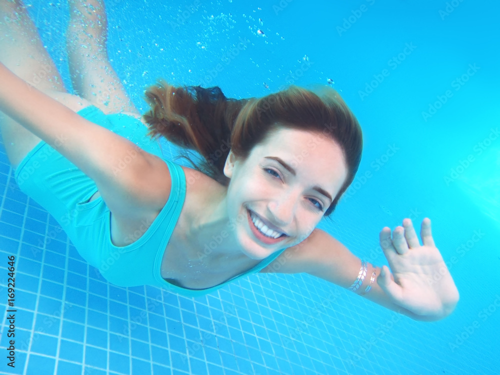 Wall mural Beautiful young woman swimming under water in pool