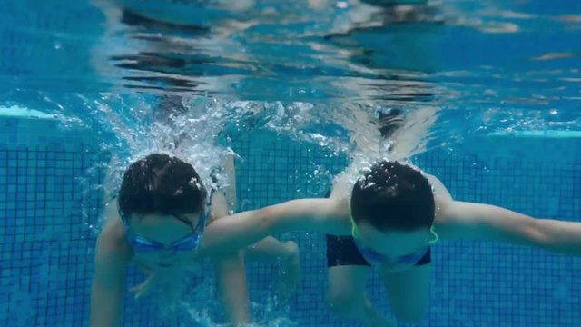 Sibling children dive into outdoor swimming pool in slow motion