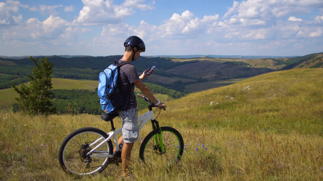A young man on a bicycle is guided by the terrain using a map on his mobile phone