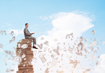 Man student on stack reading book and symbols flying around