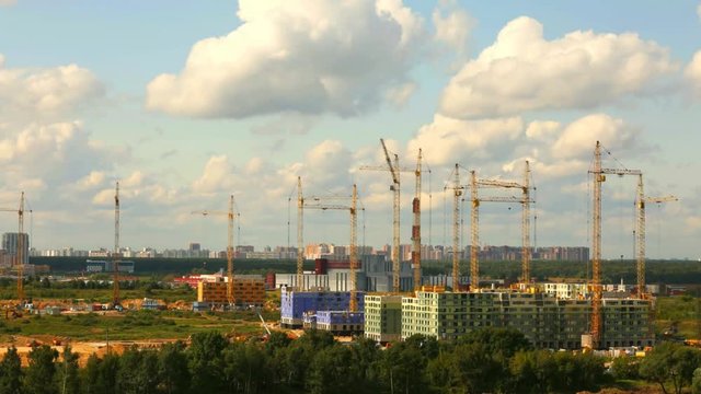 Building construction in a day time with many cranes on horizon Time lapse. Construction site with motion cranes and white clouds in blue blue sky in day time.