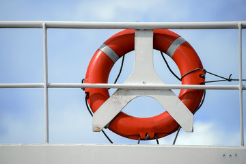 life belt, life buoy, red rescue ring on a white railing of a cruise ship against the blue sky with...