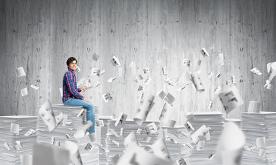 Attractive man sitting on pile of paper documents.