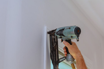 Carpenter using nail gun to moldings on windows, framing trim,