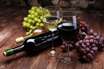Red Wine bottle and white wine with grapes and glasses on wooden background