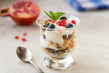 Cup of breakfast healthy muesli with blueberries, seeds of pomegranate and yogurt.