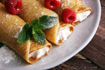 Homemade crepes served with fresh raspberrries and powdered sugar on rustic wooden table