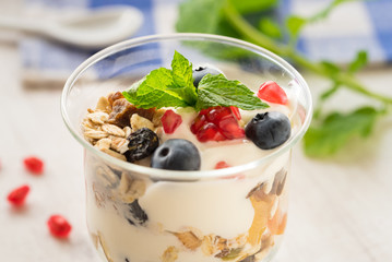 Cup of breakfast healthy muesli with blueberries, seeds of pomegranate and yogurt.