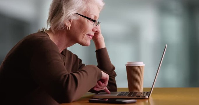 Portrait of mature businesswoman sitting at desk working on laptop. Happy Caucasian woman in her 50s scrolling through computer inside office smiling, slowmo. 4k  