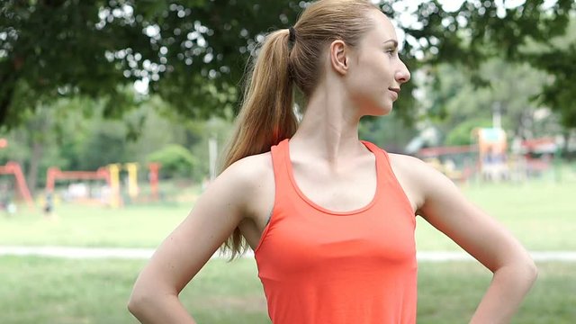 Sporty girl standing in the park and stretching her neck, steadycam shot
