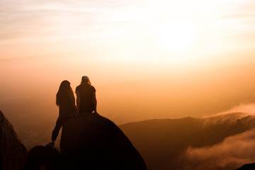 Girls sit on top of a rock during a sunrise