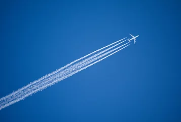 Fototapeten Ein Düsenflugzeug, das diagonal mit Kondensstreifen über Kopf fliegt. © Mark