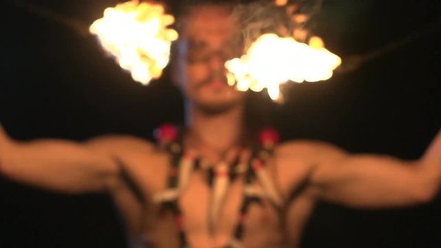 Fire show performance. Man is spinning poi on the black background and beat them from his face close to camera.