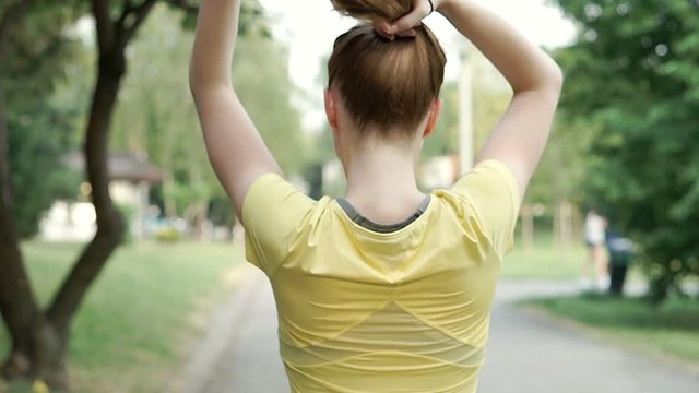 Girl standing back on the pathway and combing her hair into ponytail, steadycam shot
