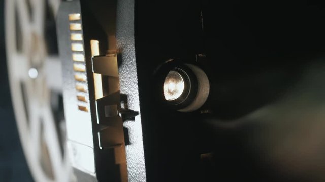 Front view of an old-fashioned antique Super 8mm film projector, projecting a beam of light in a dark room next to a stack of unraveled film reels.