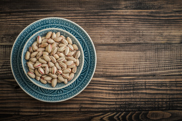 Pistachios in shell on blue plate over wooden background, top view