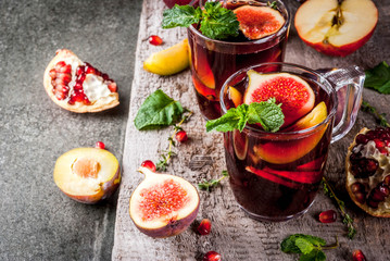 Warming autumn, winter cocktail drinks recipes. Hot red fruit sangria with apples, plums, figs, pomegranate, mint, cinnamon, thyme, lemon. On dark stone table, with wooden cutting board, copy space