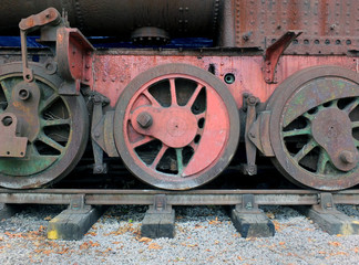wheels on an old rusting abandoned steam locomotive with red and green faded paint on tracks