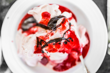 Soft serve vanilla ice cream with red strawberry sauce and drizzled chocolate syrup closeup in bowl