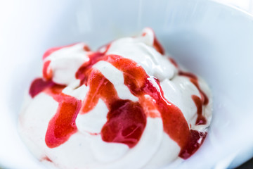 Soft serve vanilla ice cream with red strawberry sauce closeup in bowl