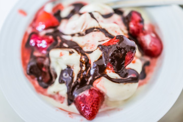 Soft serve vanilla ice cream with red strawberry sauce and drizzled chocolate syrup closeup in bowl flat top view