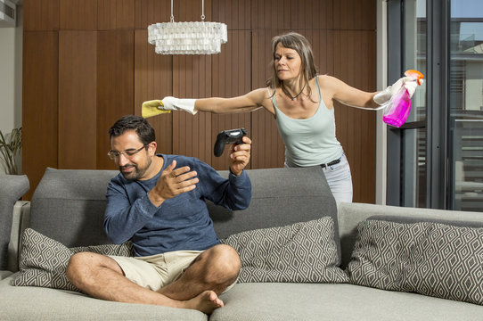 arab man playing a video game while woman is cleaning around him