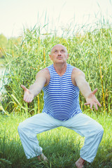 Naklejka na ściany i meble Older man is engaged in gymnastics in nature on a bright sunny day with a good mood and faith in herself. Morning exercise and healthy lifestyle