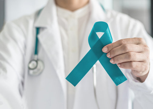 Teal awareness ribbon in doctor's hand, symbolic bow color for supporting patient with Ovarian Cancer, PCOS and PTSD Illness