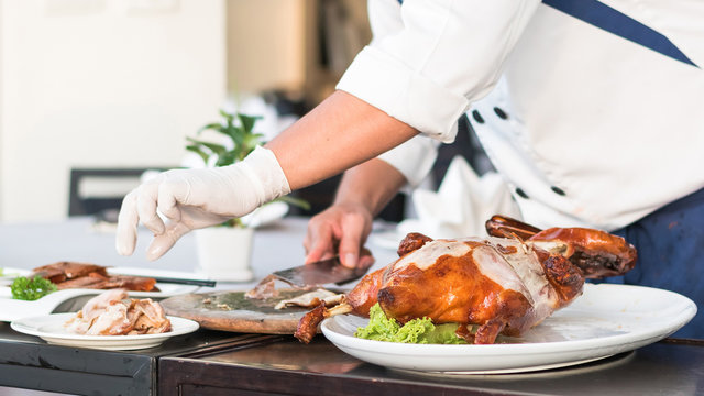 Chef preparing Chinese Peking Duck on dishes for food serving on restaurant table