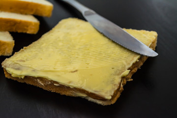 Butter with beautiful stains and a knife on a piece of bread close-up on a dark background