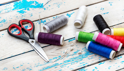 Sewing threads with scissors, needles and pins on the old wooden background.