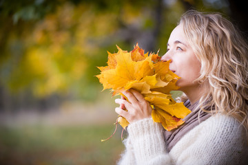 Portrait of young woman with maple leaves on autumn sunset background. Girl walking in the park and enjoying sunny weather. Lifestyle and autumn concept
