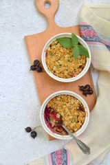 Fruits casserole or crumble with apples and berries in brown cup ramekin on light background. Copy space. Photographing with natural light