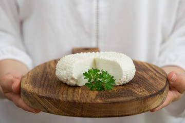 Closeup of woman's hand holding round white homemade cheese  - traditional milk creamy dairy product on vintage wooden board. Rustic style.