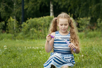 Little child girl playing with soap bubble in summer park