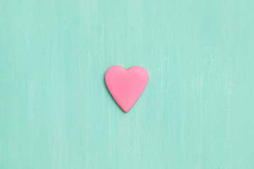 Fototapeta premium Top view on a pink gingerbread cookie in shape of heart on turquoise background. Flay layout. Love, Valentines's day concept
