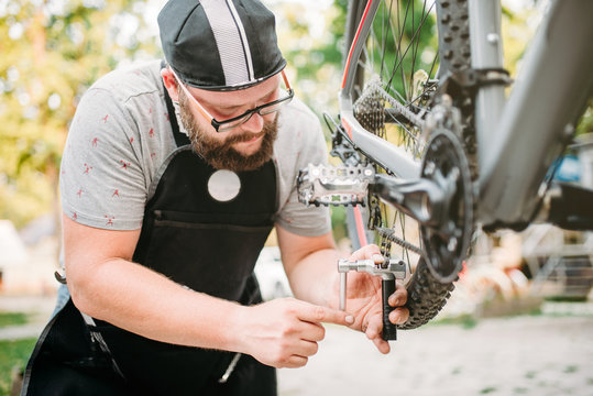Bicycle mechanic in apron adjusts bike chain