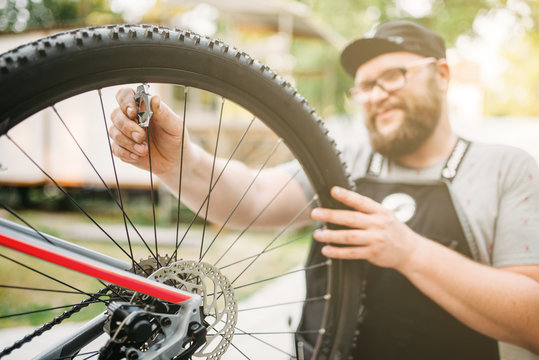 Bicycle mechanic in apron adjusts bike spokes 