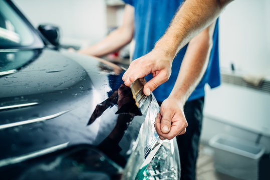 Worker hands wraps car hood in protective coating