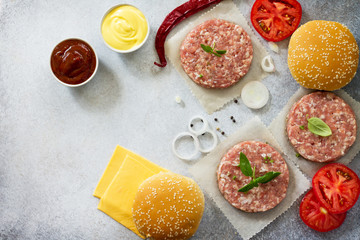 Cheeseburger cooking. Ingredients for cheeseburger - raw cutlets, tomato sauce, cheese sauce, bun, cheese, onion, spices, greens and tomatoes. Fast food. Top view with a copy.