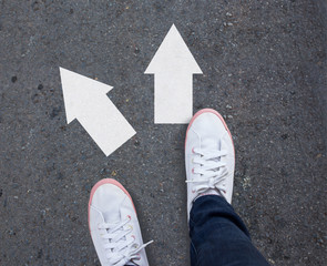 Pair of shoes standing on a tarmac road with two arrows