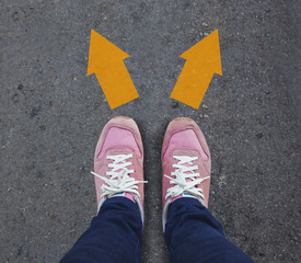 Pair of shoes standing on a tarmac road with two arrow