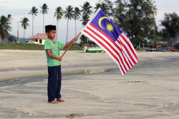 The Concept of Independence Day - a boy holding the Malaysian flag on the shore