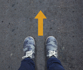 Pair of shoes standing on a road with yellow arrow.