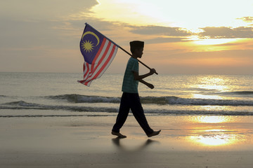 The Concept of Independence Day - a boy holding the Malaysian flag on the shore at sunrise