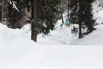 Fototapeta premium Young girl snowboarder goes towards camera on snowy mountain in the forest