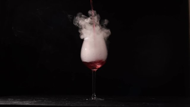 Person pours wine into glass with liquid nitrogen on black background