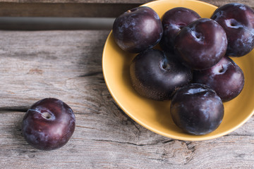 a yellow plate on the wood with many plums