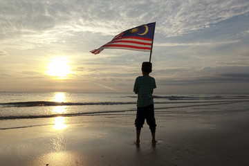 The Concept of Independence Day - a boy holding the Malaysian flag on the shore at sunrise